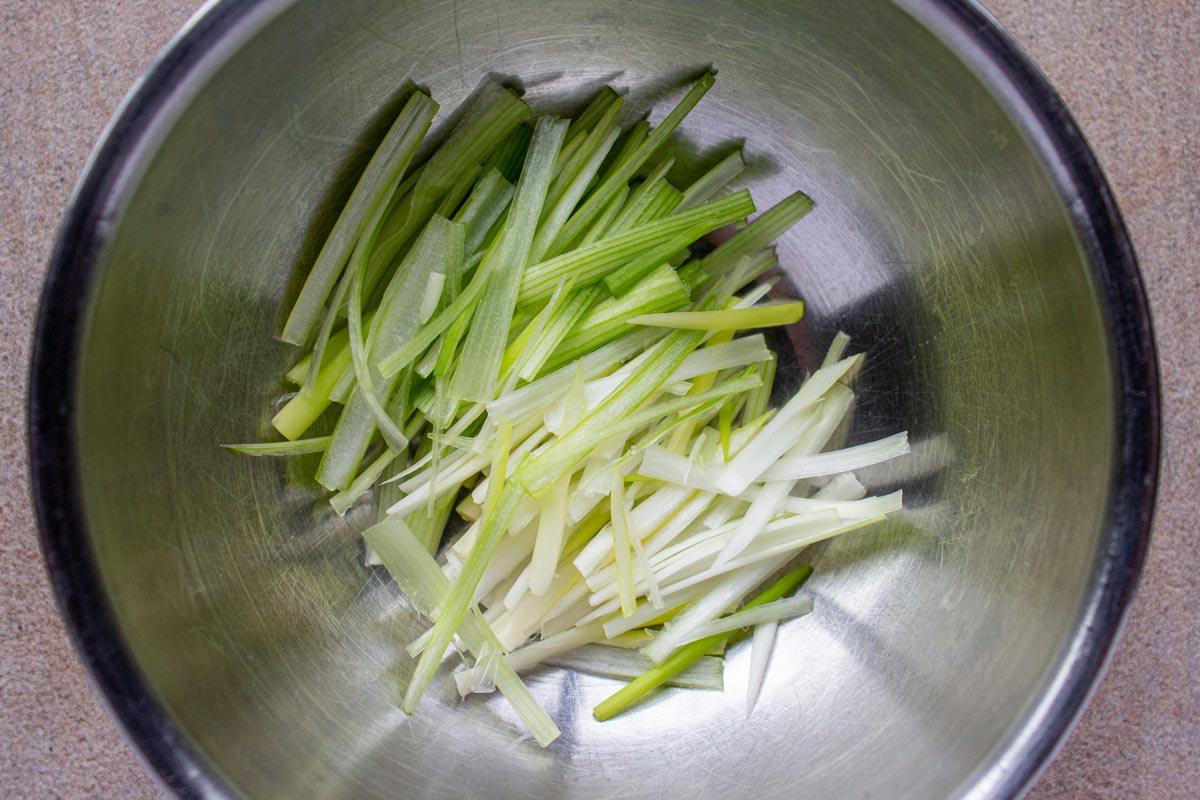 Slivers of light green and white scallion in a metal bowl.