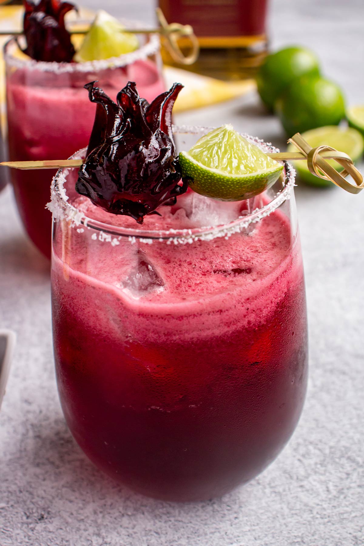 Closeup of a pink margarita in a short glass garnished with a lime wedge and hibiscus.