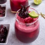 Closeup of a dark pink hibiscus margarita garnished with skewered lime and hibiscus flower.