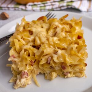 A square piece of cheesy German ham and noodle casserole on a white plate.
