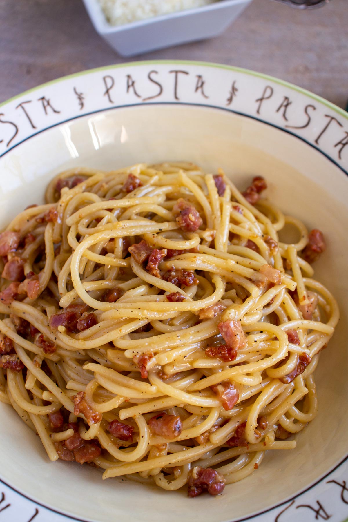 Spaghetti with crispy pancetta in a wide bowl that says pasta around the edges.