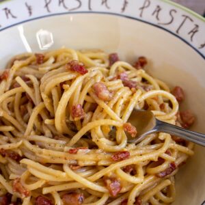 Closeup of spaghetti alla carbonara twirled around a fork resting in a dish of spaghetti.