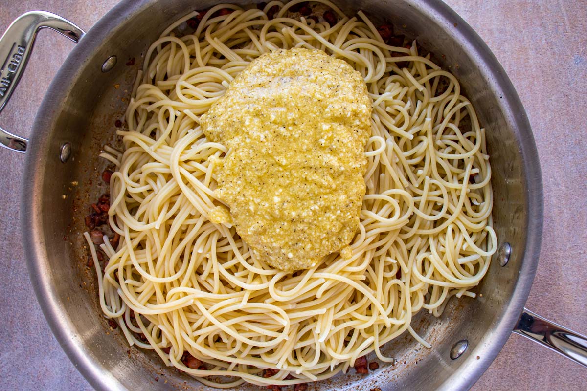 A metal skillet filled with cooked spaghetti and topped with a beaten egg and cheese mixture.