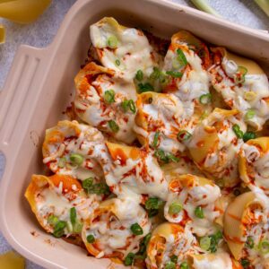 Baked buffalo chicken stuffed shells topped with scallions and arranged in a rectangular baking dish.