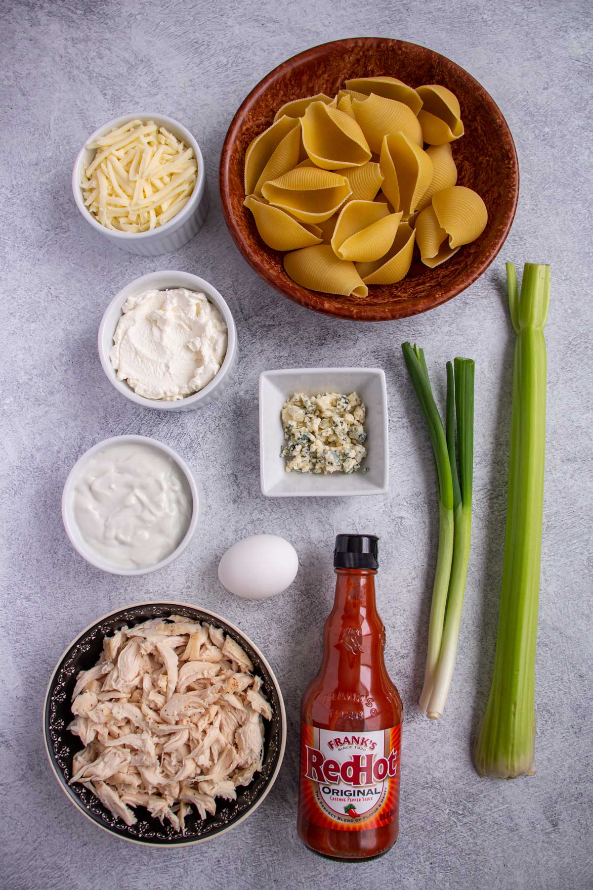 Ingredients for buffalo chicken stuffed shells on a grey concrete background.
