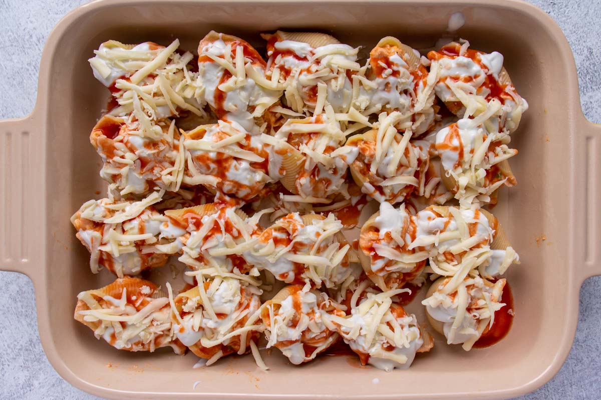 Jumbo pasta shells in a baking dish topped with white and red sauces and shredded cheese.