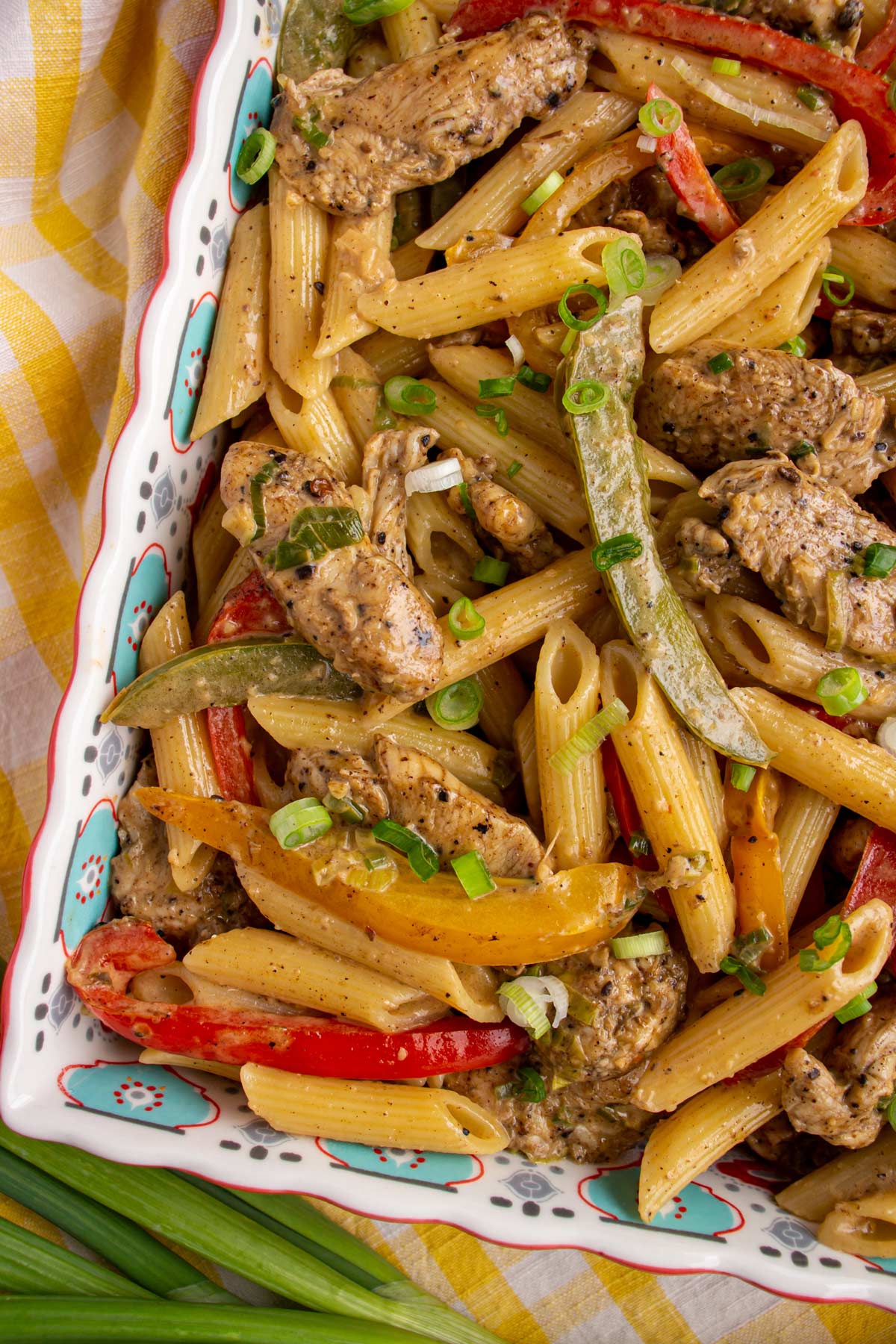 Penne pasta with jerk chicken pieces and colorful sliced peppers in a square serving dish.