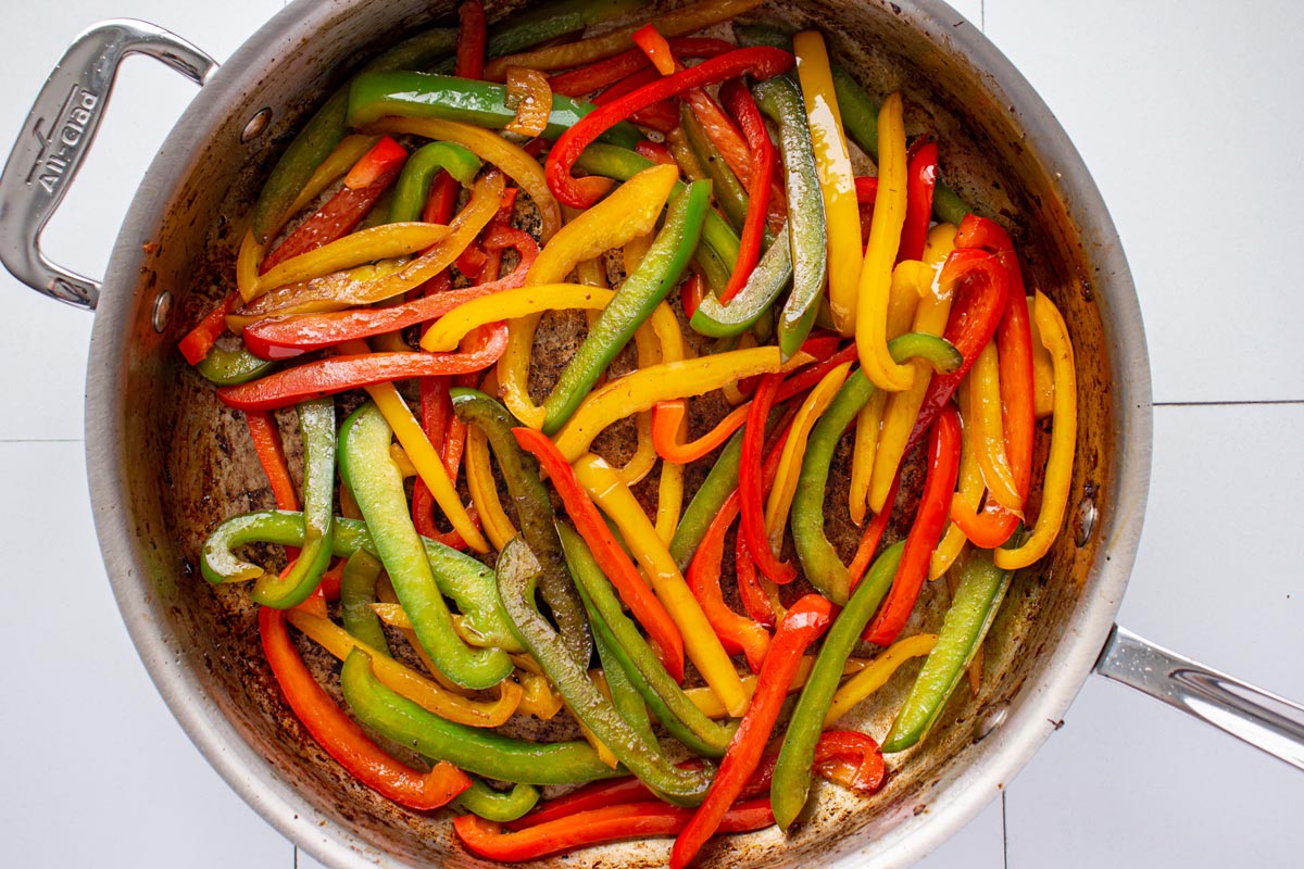 Slices of cooked red, yellow, and green bell pepper in a stainless steel skillet.