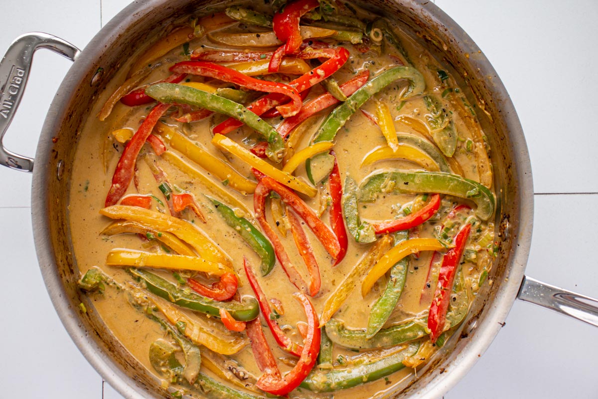 Colorful cooked pepper slices in a light brown creamy sauce in a metal skillet.