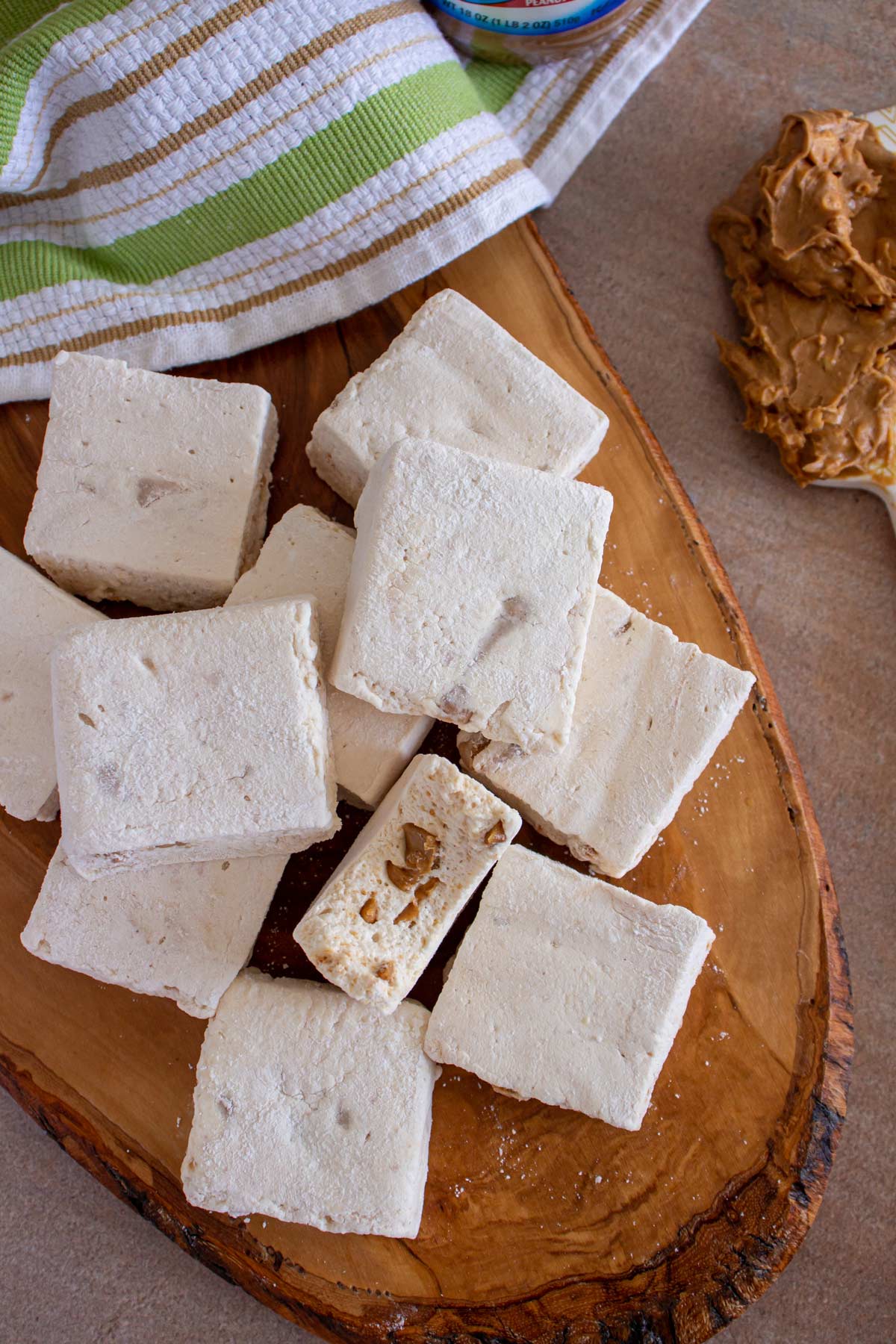 Square marshmallows with one partially eaten piled on an oval wooden board.