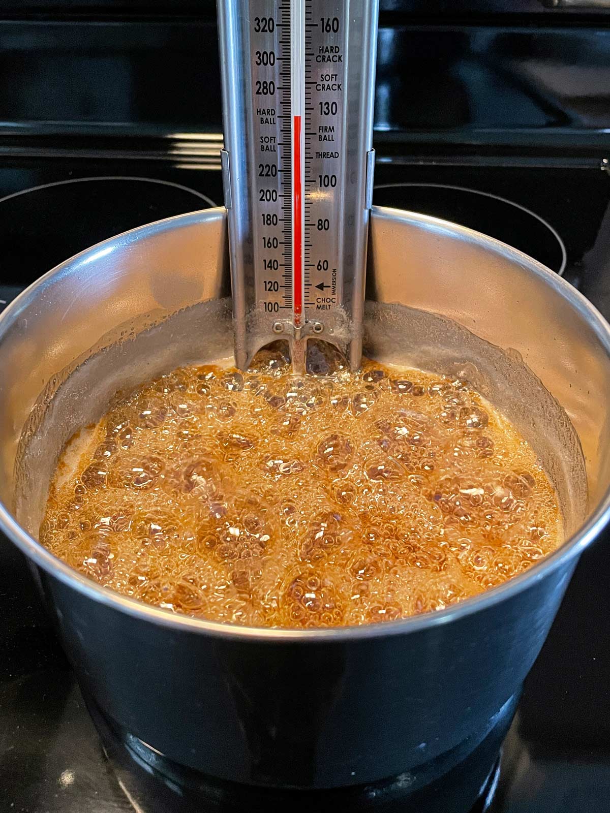 Sugar syrup cooking in a saucepan with a candy thermometer clipped in the back.