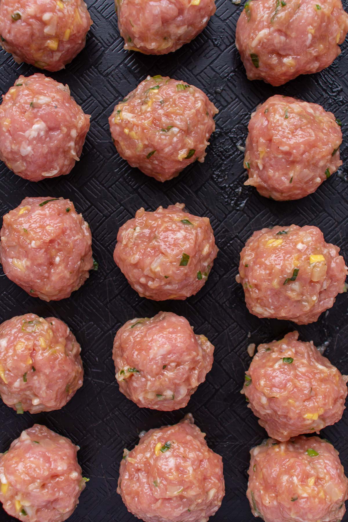 Small uncooked meatballs arranged in rows on a black surface.