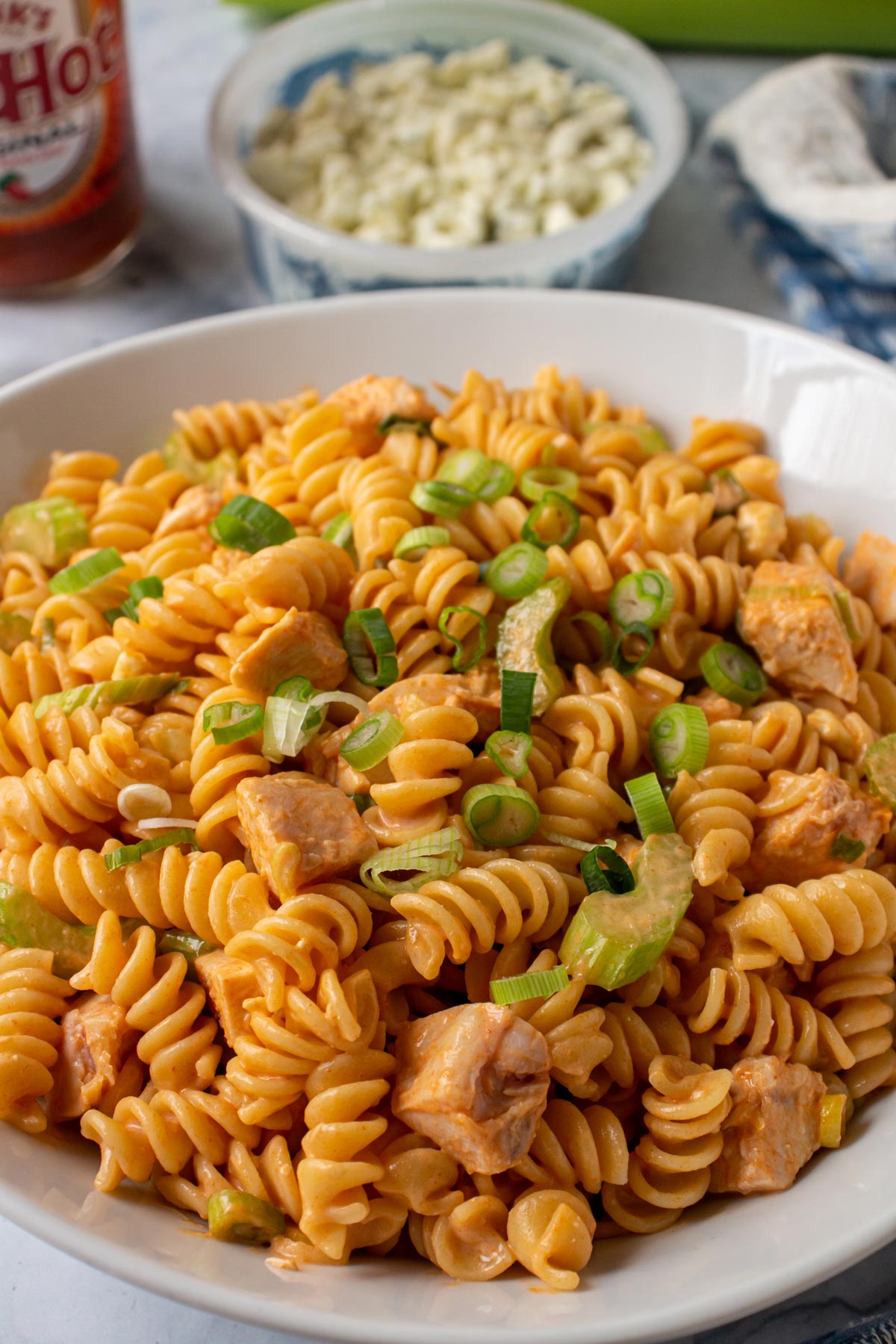 Pasta salad with Buffalo dressing, chicken, and celery in a white serving bowl.