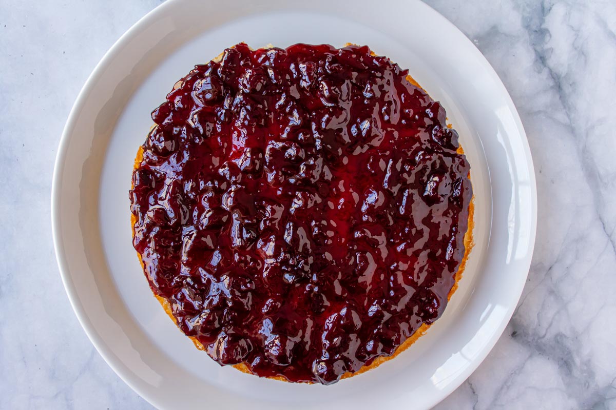 Cherry preserves spread over a cake layer on a white plate.