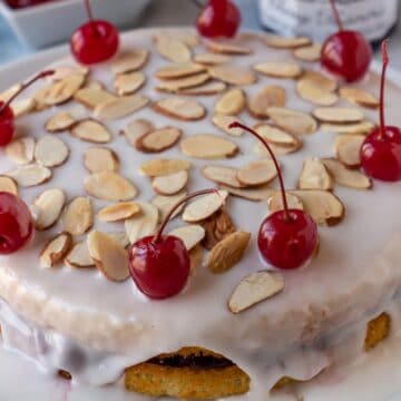A layer cake topped with white glaze, sliced almonds, and cherries.