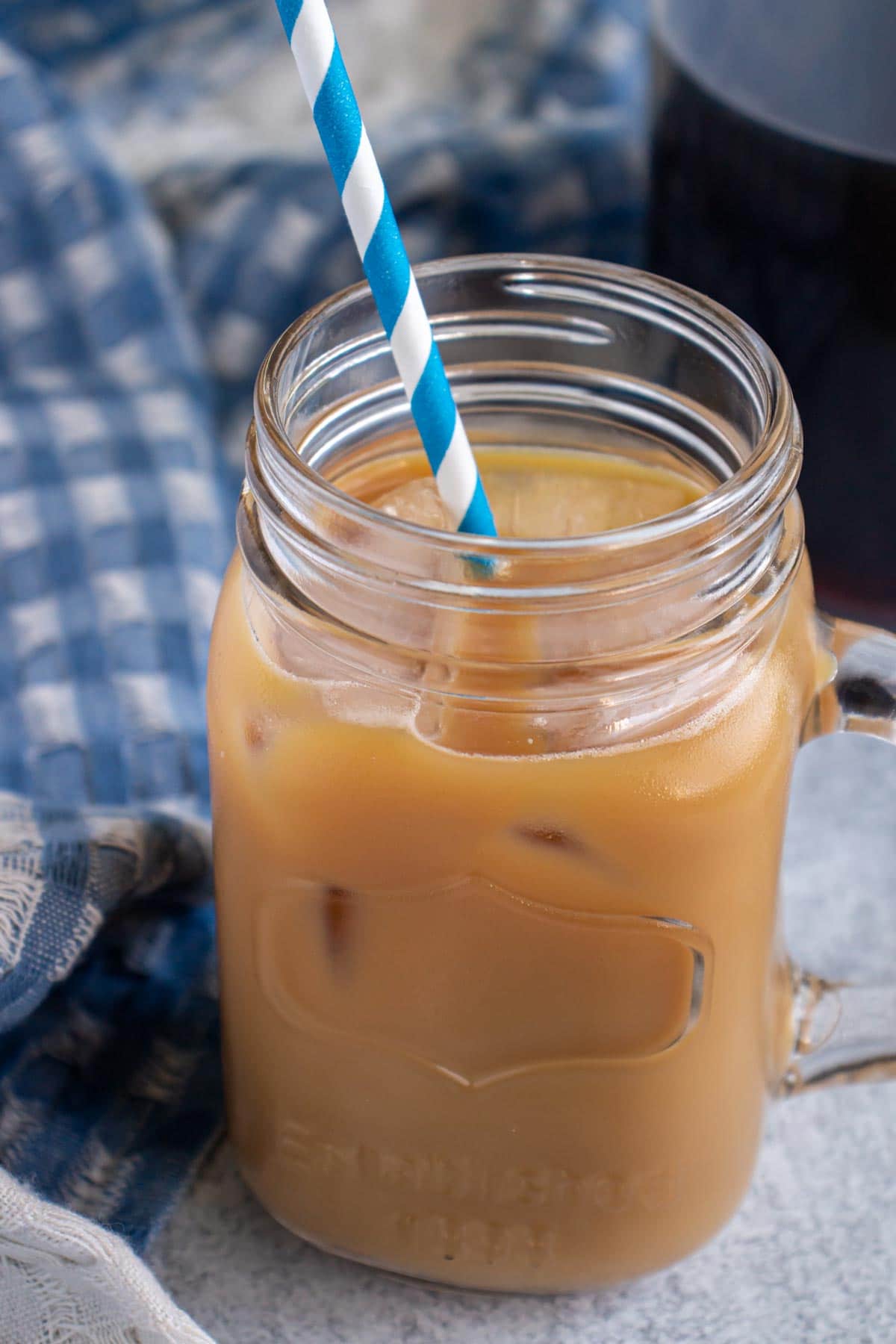 A glass mug filled with iced coffee next to a blue and white checkered towel.