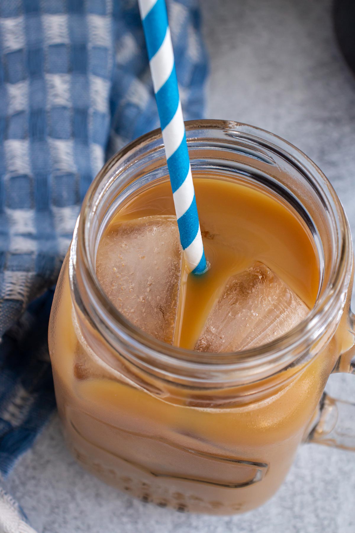 A glass mug filled with cold brew coffee with a blue and white striped straw.