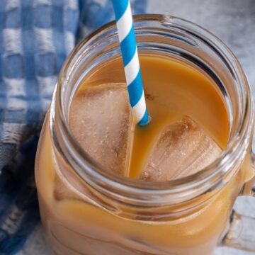 A glass mug filled with cold brew coffee with a blue and white striped straw.