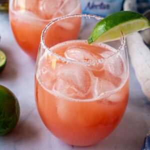 A guava margarita in a salt-rimmed glass garnished with a lime wedge.