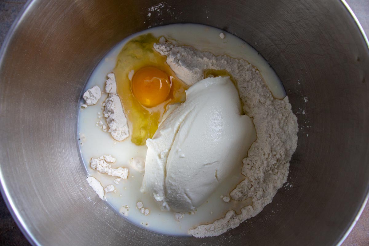 Flour, ricotta cheese, egg, and milk in a metal mixing bowl.