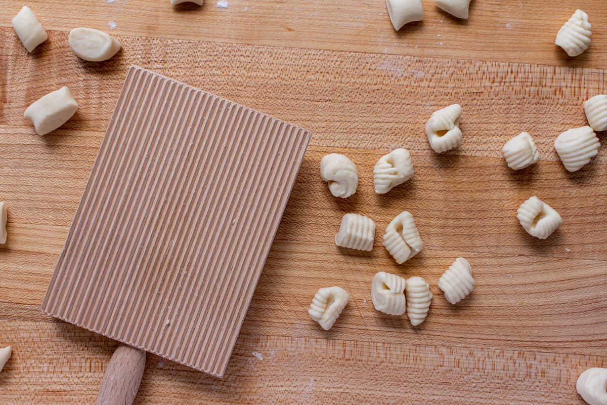 Small pieces of dough, rolled ricotta cavatelli and a gnocchi board on a wooden surface.