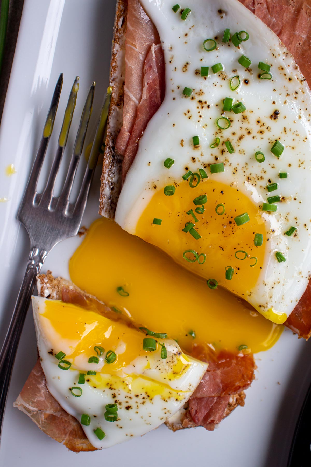 A sandwich topped with a fried egg, cut to release the egg yolk onto the plate.