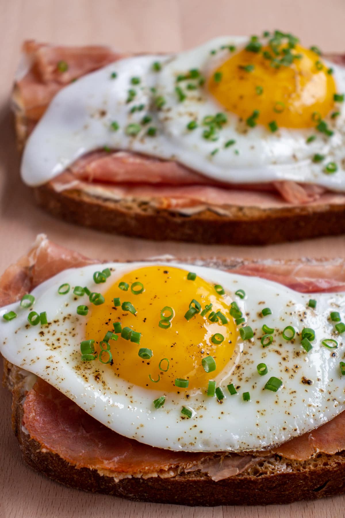 Closeup of two Strammer Max open-faced sandwiches with prosciutto and egg on a wooden board.