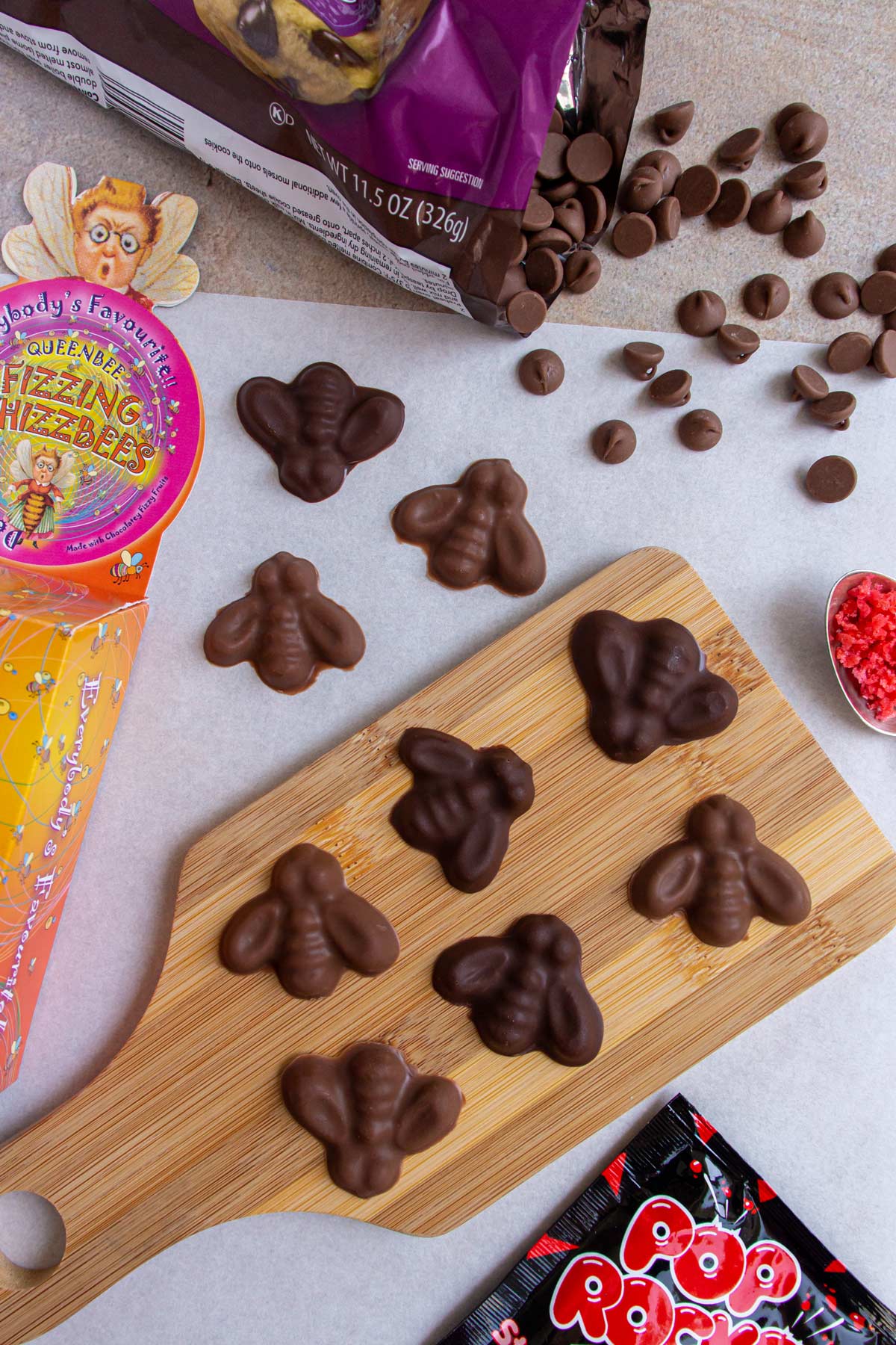 Bee shaped chocolates on a small wooden board, chocolate chips, and a package of Pop Rocks.