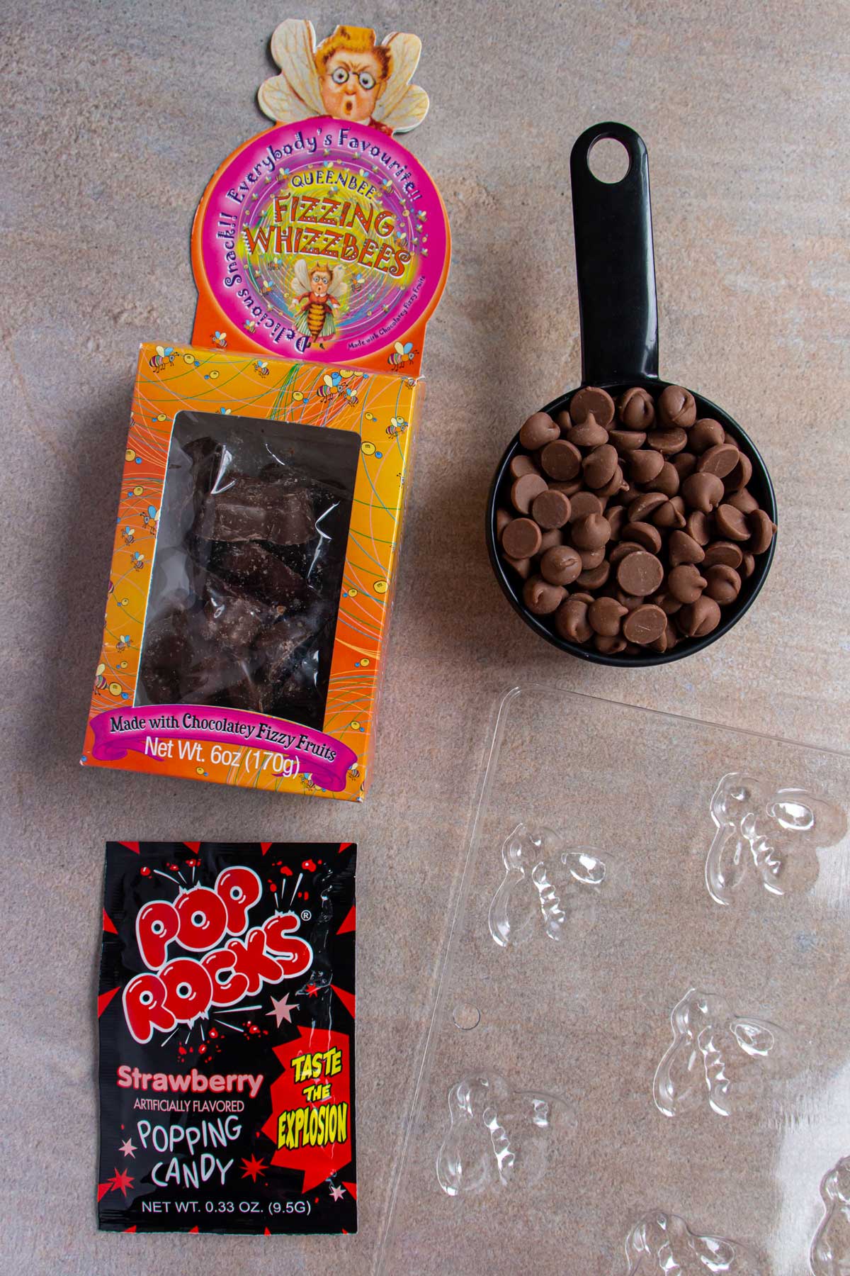 A box of Fizzing Whizzbees candy, chocolate chips, Pop Rocks, and a plastic bee candy mold.