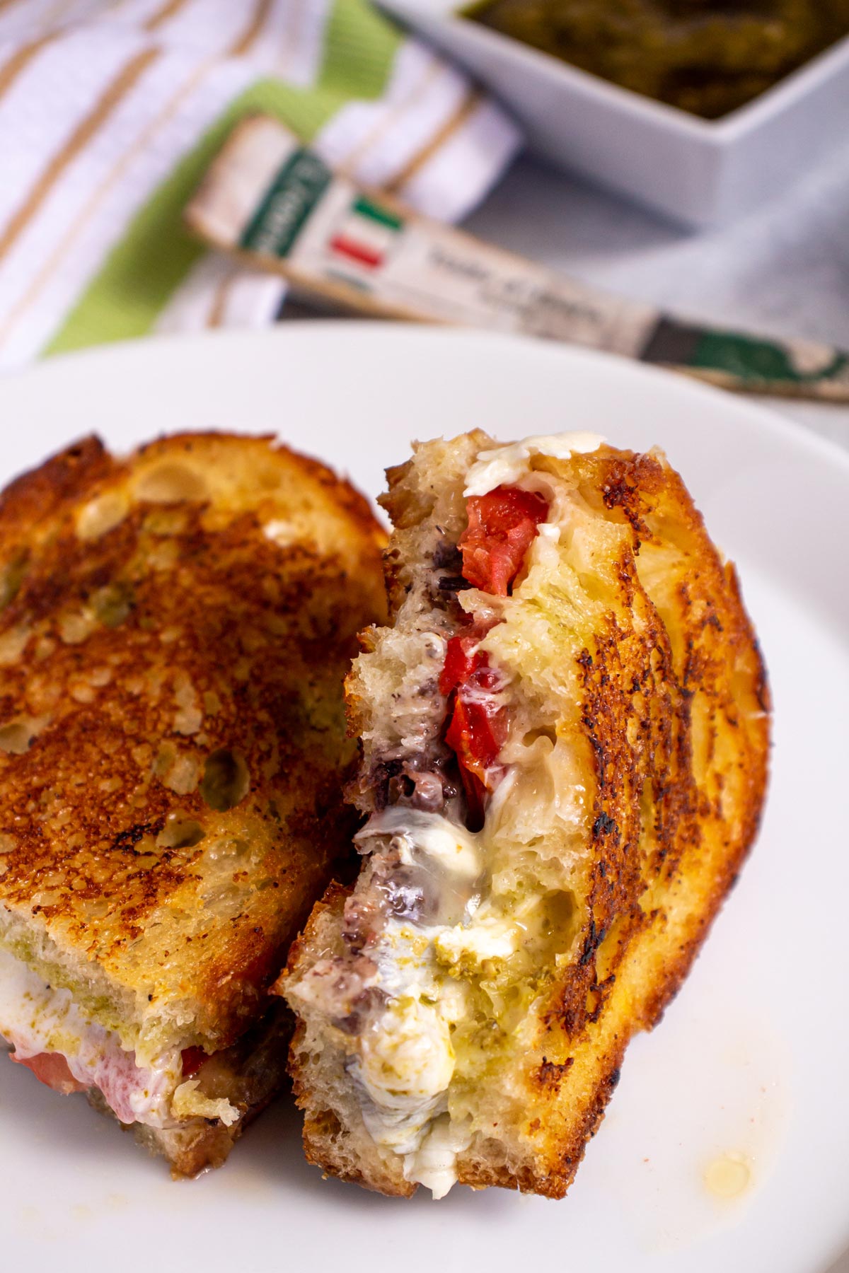 Closeup of a half-eaten grilled cheese sandwich with tomato, pesto, and olive tapenade.