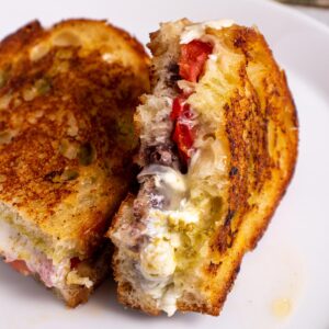 Closeup of a half-eaten grilled cheese sandwich with tomato, pesto, and olive tapenade.