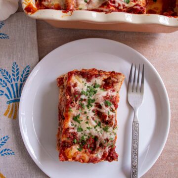 A slice of lasagna on a white plate with a fork.