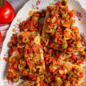 Fish fillets topped with a tomato, olive, caper sauce on an oval platter.