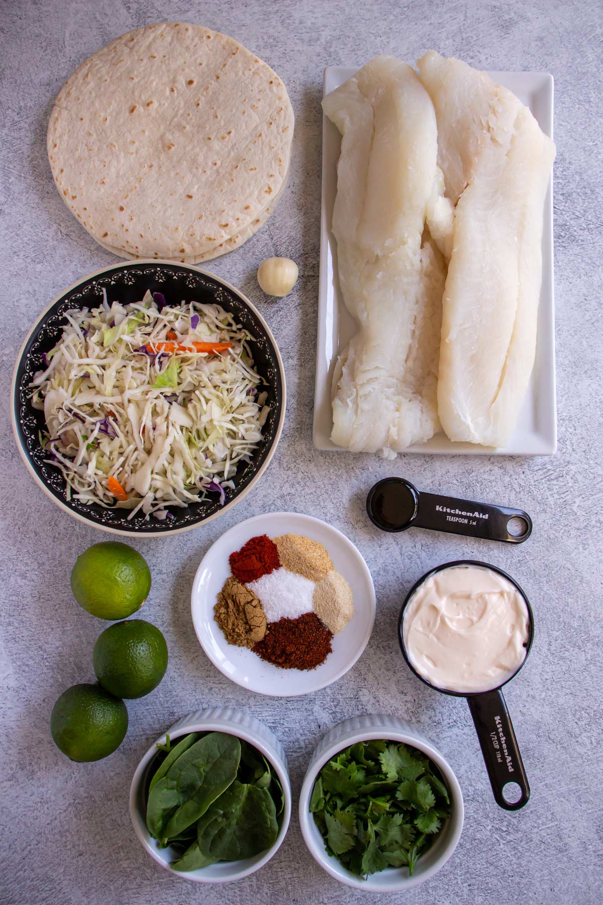 Ingredients for grilled fish tacos on a greyish white background.