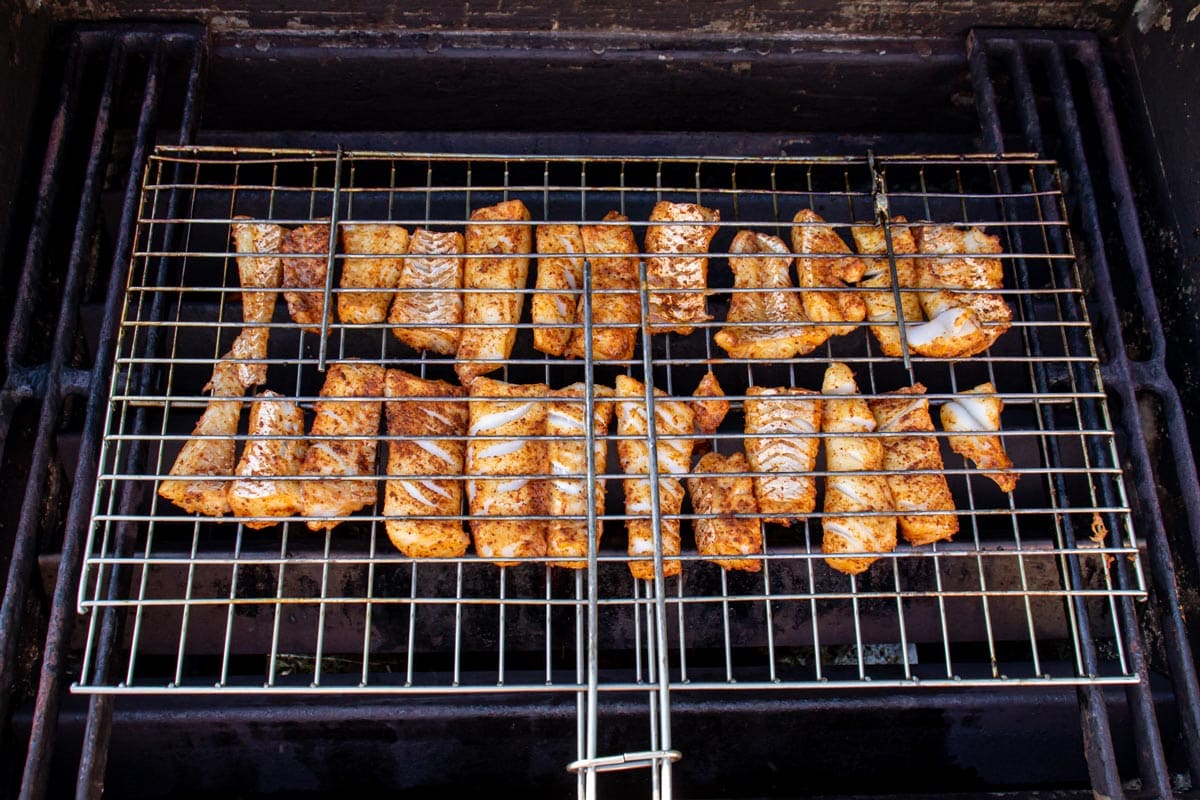 Strips of fish in a fish grill basket set on a gas grill.