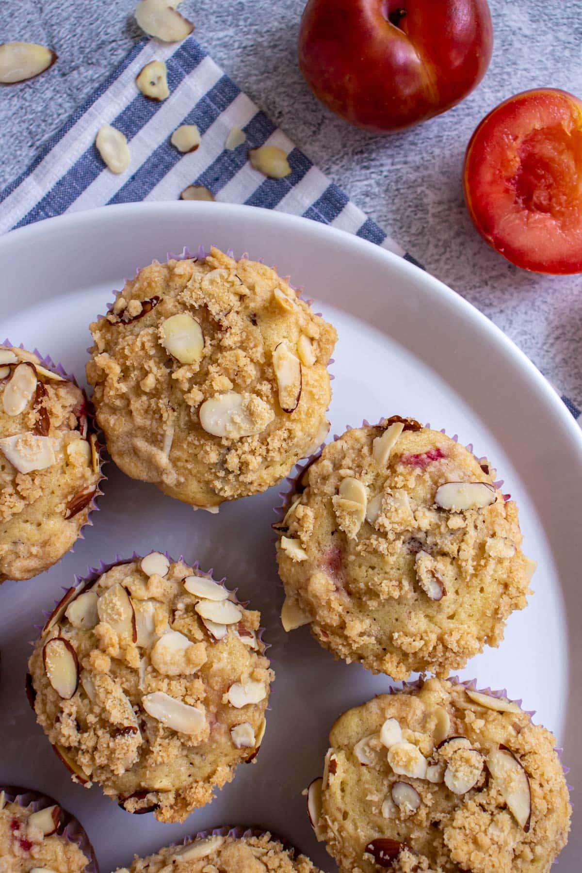 Muffins on a round white plate with sliced almonds and plums next to the plate.