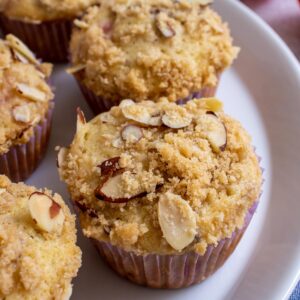 A plate of plum almond muffins with streusel and sliced almonds on top.