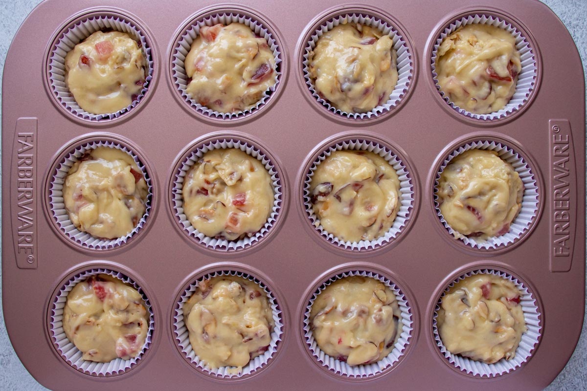 Twelve muffin cups in a muffin pan filled with plum almond muffin batter.