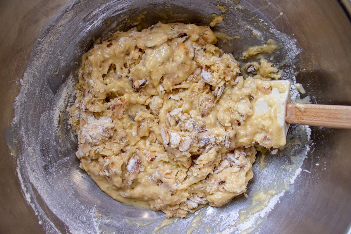 Muffin batter with streaks of flour showing, in a metal mixing bowl with a rubber spatula.