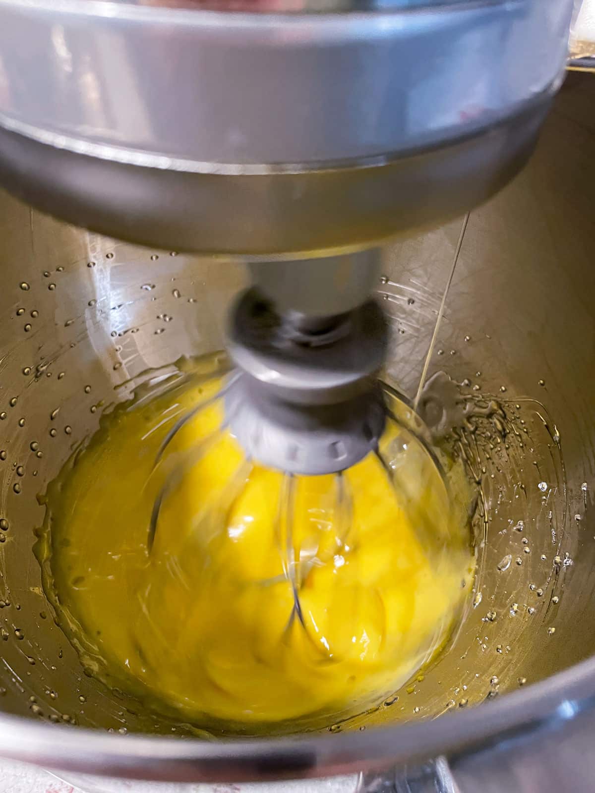 Process of pouring hot syrup down the side of a mixer bowl and beating into eggs.