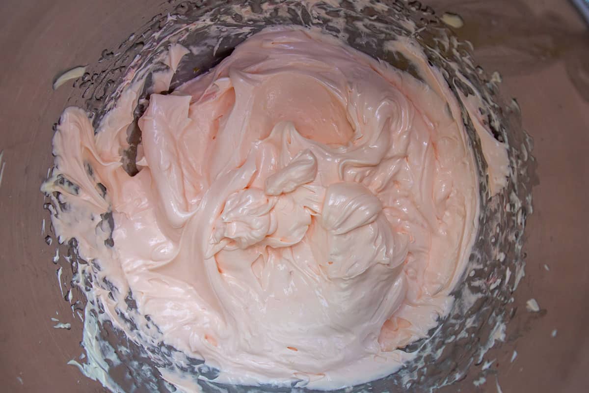 French buttercream frosting tinted pink in a metal mixing bowl.