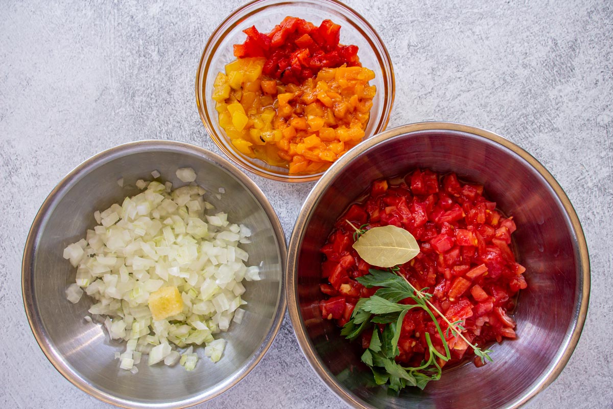 Three bowls with diced roasted peppers, diced tomato with herbs, and diced onion with garlic.