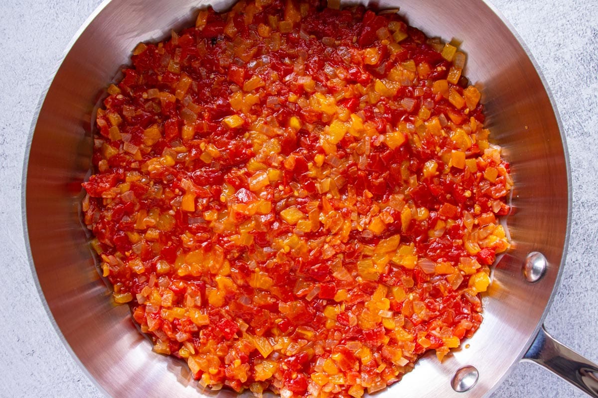 Red and orange hued piperade bell pepper sauce spread evenly in a stainless steel skillet.