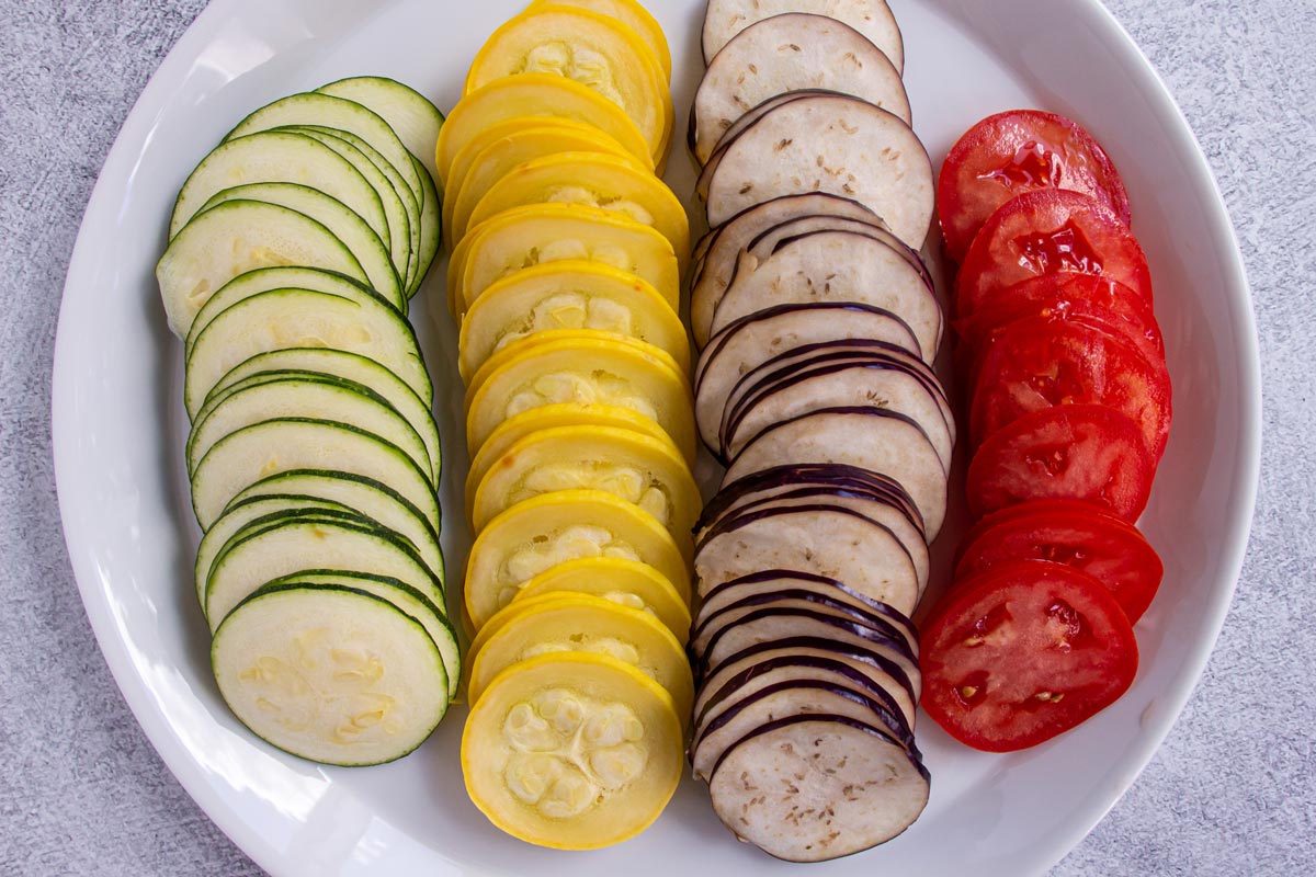 Very thinly sliced zucchini, summer squash, Japanese eggplant, and tomato arranged in rows.