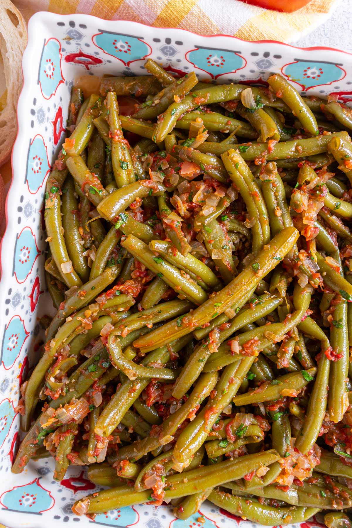 Closeup of stewed green beans with tomato sauce in a square serving dish.