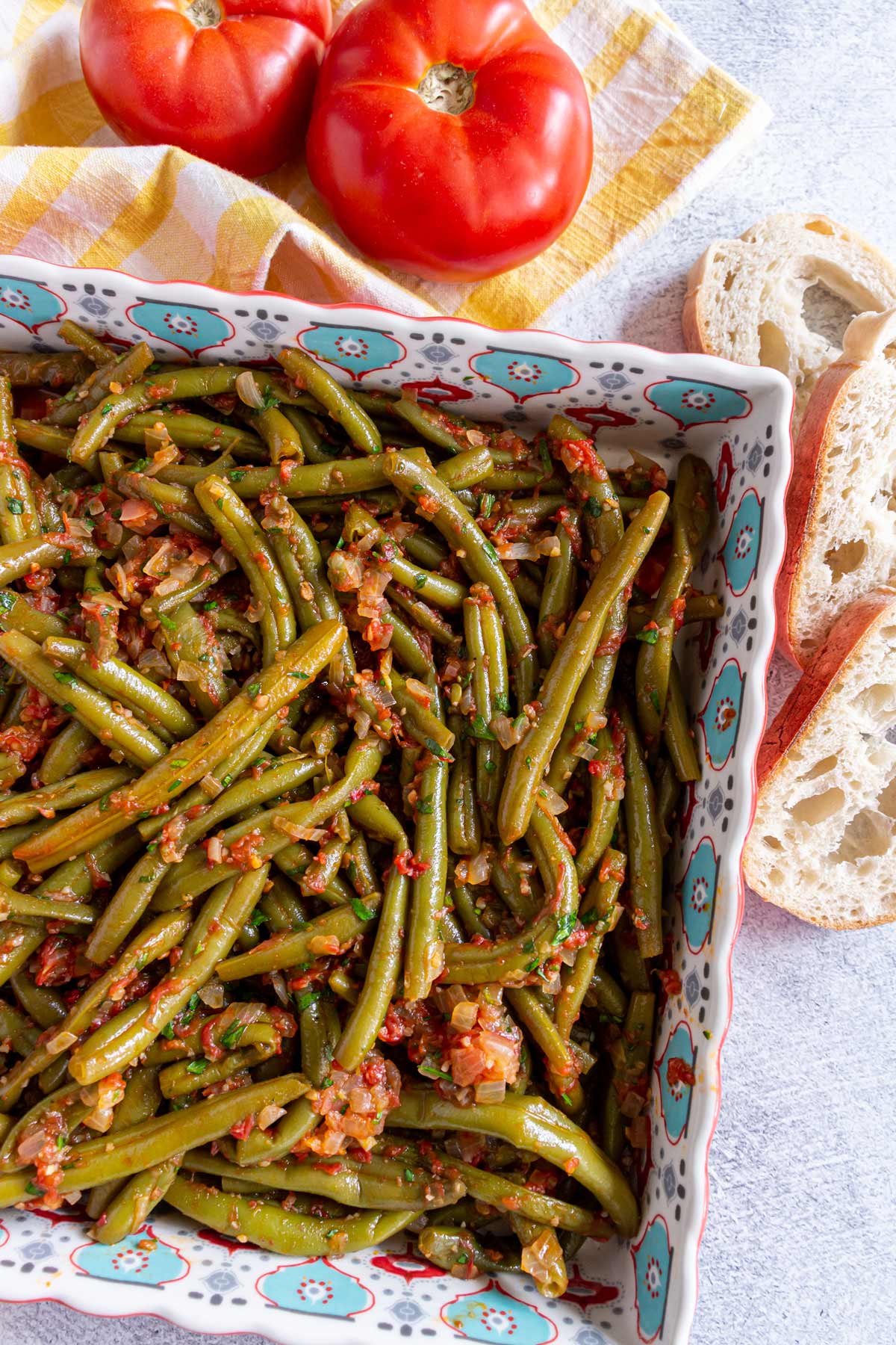 Greek stewed green beans in a square dish with sliced bread and tomatoes next to it.