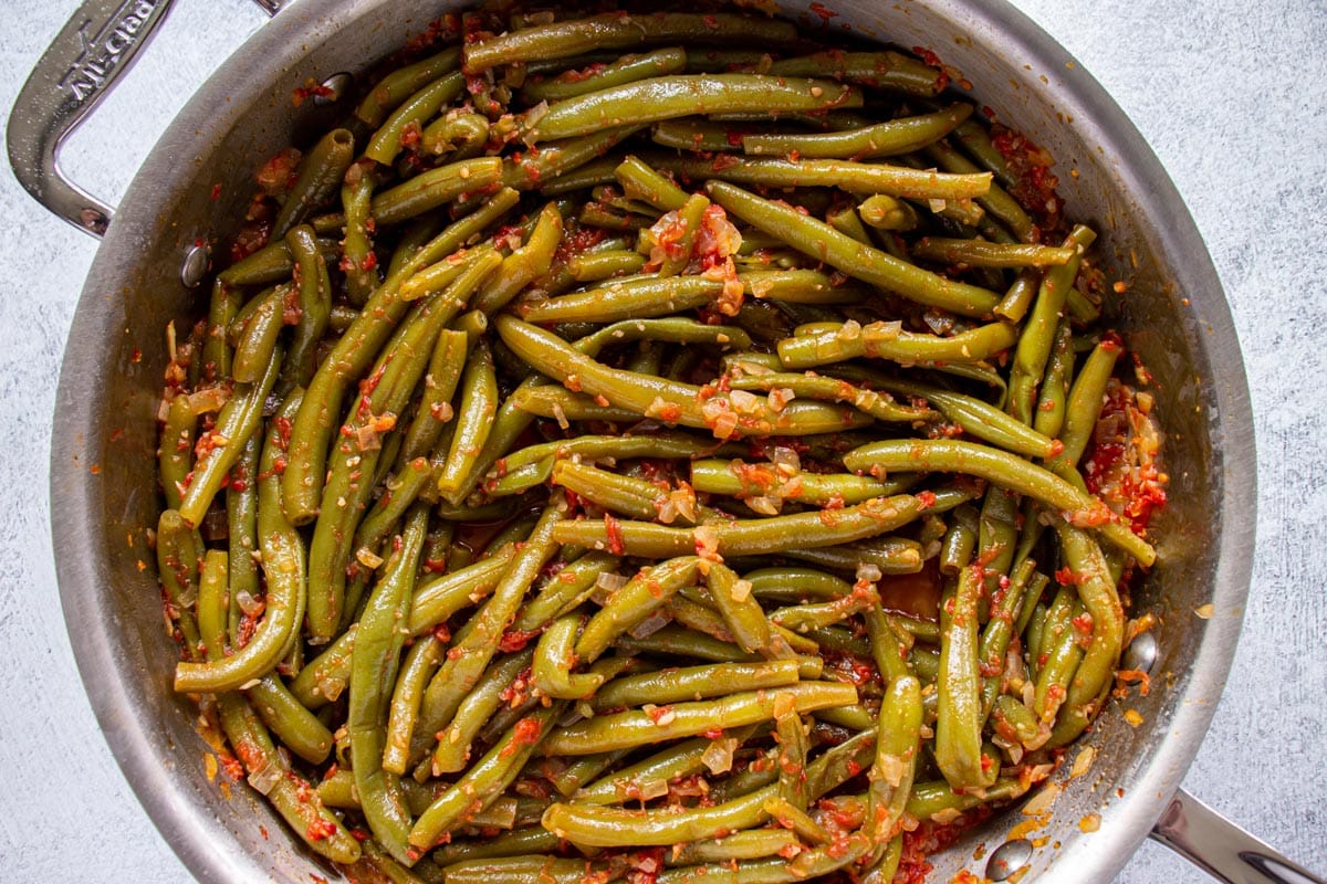 Cooked green beans in a tomato sauce in a stainless steel pan.