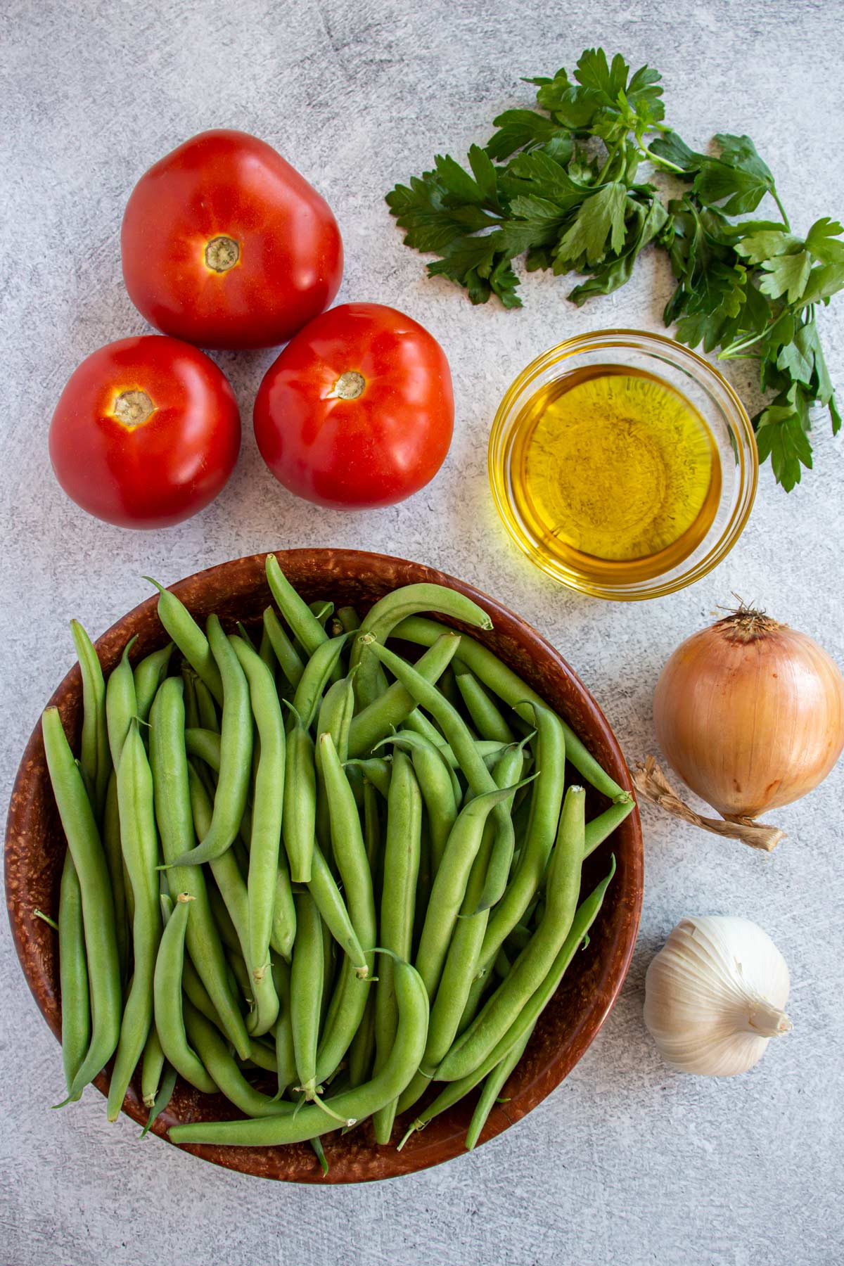Ingredients for fasolakia Greek green beans on a light grey background.