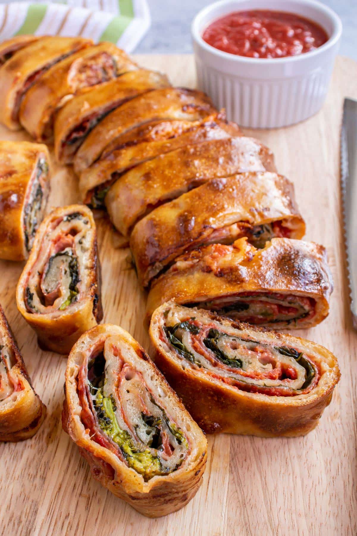 A sliced Italian stromboli with soppressata and rapini filling arranged on a wooden board.