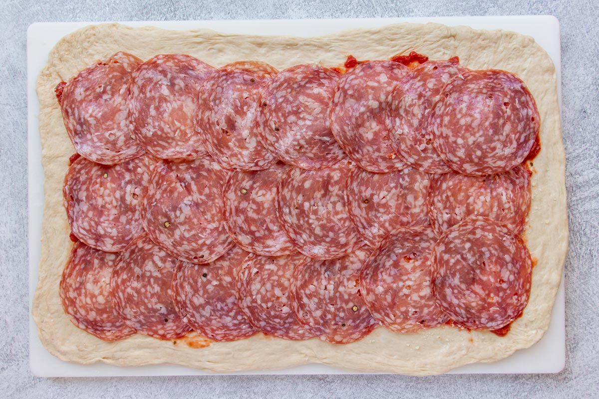 Sliced soppressata salami arranged over the top of a rectangular pizza dough.